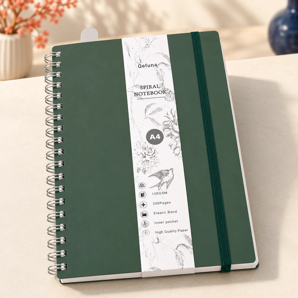 Qefuna — cahier vert de 300 pages à spirale de Qefuna, mise en situation dans un atelier de papier écru et corail
