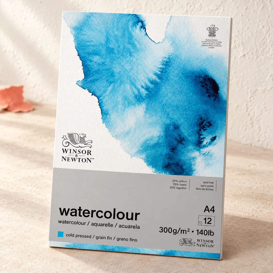 Winsor & Newton — aquarelle A4 à 25 % coton de Winsor & Newton, mise en situation dans un atelier de papier écru et corail